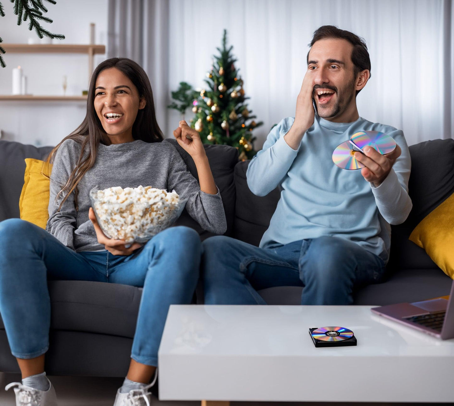 Afbeelding van een man en vrouw die popcorn eten en een film kijken - de externe dvd/cd-speler staat op tafel - ze lachen en genieten